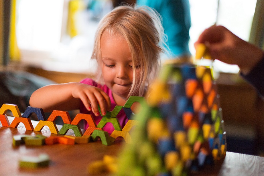 Wir helfen Ihrem Kind mit einer individuellen Therapie. Ein kleines Mädchen spielt konzentriert mit bunten Bauklötzen. Das Bild symbolisiert die ergotherapeutische Förderung von Kindern, die in ihrer Handlungsfähigkeit eingeschränkt sind, mit dem Ziel, ihre Selbstständigkeit und altersgerechte Entwicklung zu unterstützen.